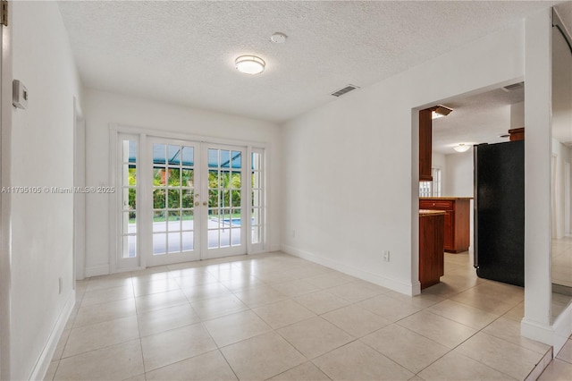 spare room featuring a textured ceiling, french doors, baseboards, light tile patterned floors, and visible vents