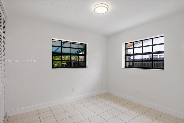 empty room featuring baseboards, light tile patterned floors, and a wealth of natural light