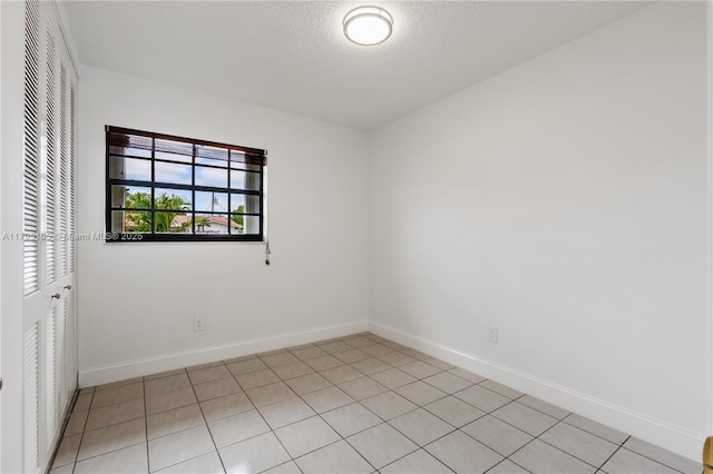 empty room with baseboards, a textured ceiling, and light tile patterned floors