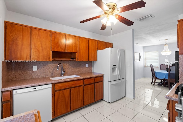 kitchen with brown cabinetry, visible vents, tasteful backsplash, a sink, and white appliances