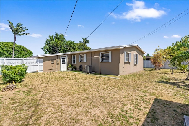 rear view of property featuring a fenced backyard, stucco siding, a yard, and central AC