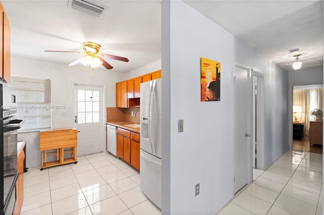kitchen with light tile patterned flooring, ceiling fan, a sink, white appliances, and visible vents