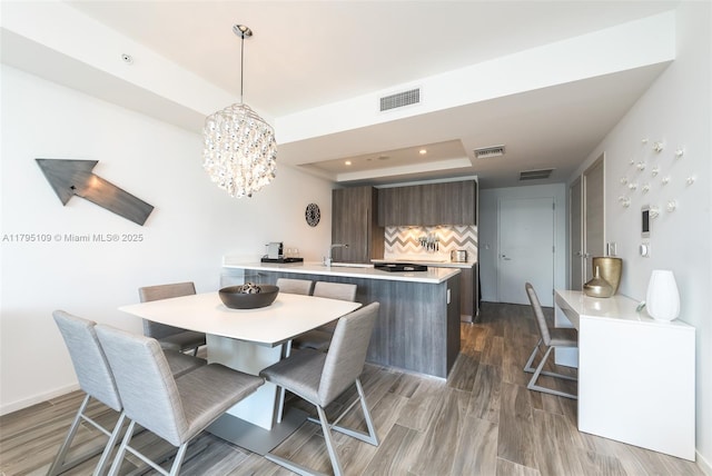 dining room with visible vents, an inviting chandelier, a raised ceiling, and wood finished floors