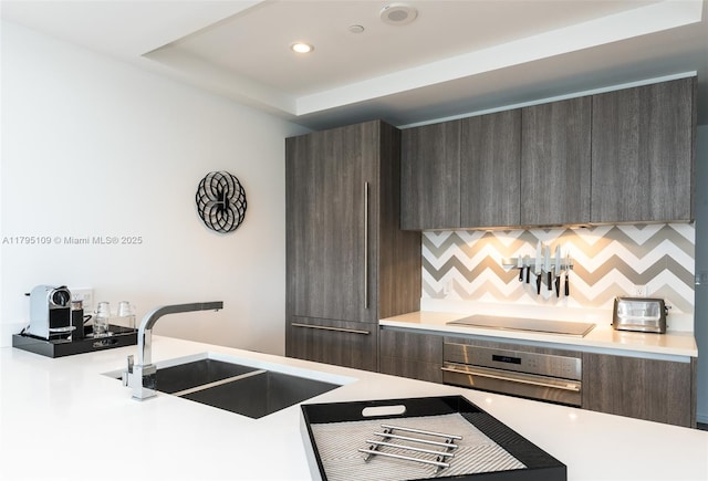 kitchen with stainless steel oven, modern cabinets, black electric stovetop, light countertops, and a sink