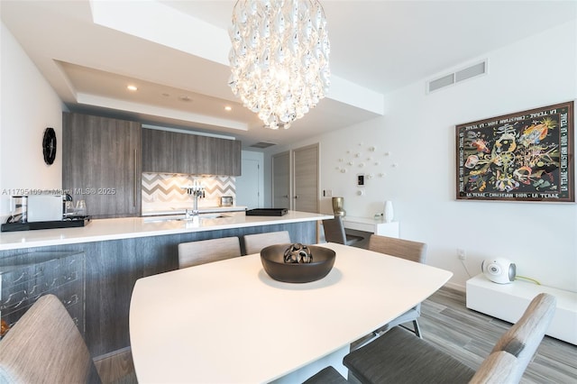 dining room with visible vents, wood finished floors, a raised ceiling, an inviting chandelier, and recessed lighting