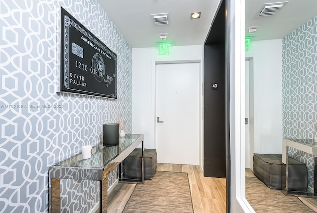 corridor with wallpapered walls, wood finished floors, and visible vents