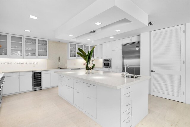kitchen with beverage cooler, a sink, appliances with stainless steel finishes, and a kitchen island with sink