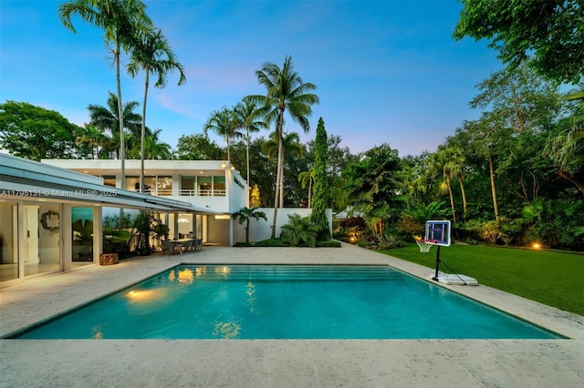 pool at dusk with a yard, a patio area, and an outdoor pool