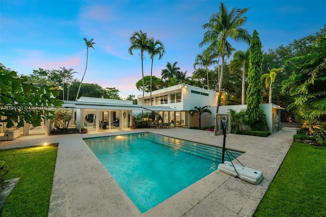 pool at dusk with a yard, a patio, and an outdoor pool
