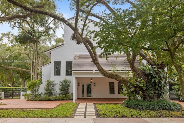view of front of house with stucco siding, french doors, a tile roof, and fence