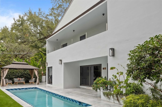 back of property featuring a gazebo, a patio, stucco siding, and an outdoor pool