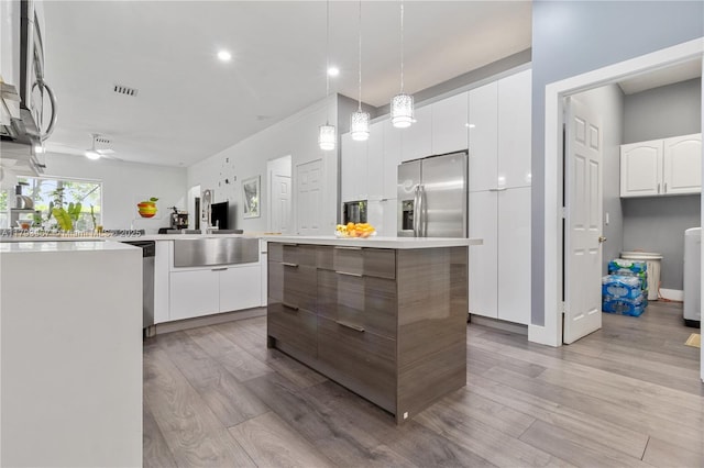 kitchen with appliances with stainless steel finishes, light wood finished floors, a sink, and visible vents