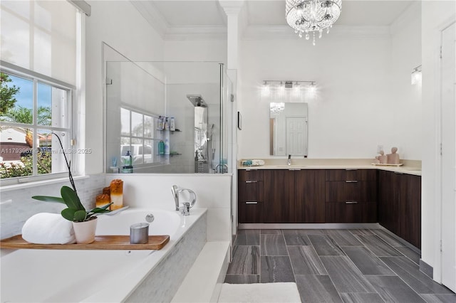 full bath with a notable chandelier, vanity, a shower stall, ornamental molding, and a garden tub