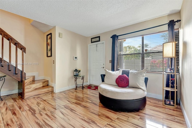 sitting room featuring stairs, a textured ceiling, baseboards, and light wood-style floors