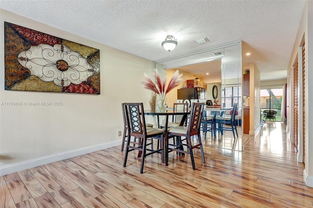 dining room with a textured ceiling, baseboards, visible vents, and light wood-style floors