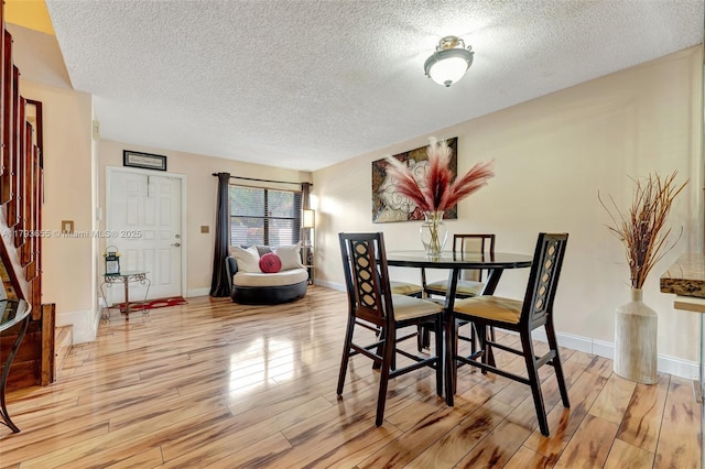 dining area with a textured ceiling, baseboards, and light wood finished floors