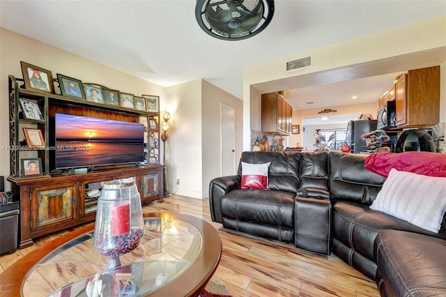 living area with a textured ceiling, light wood-style flooring, and visible vents