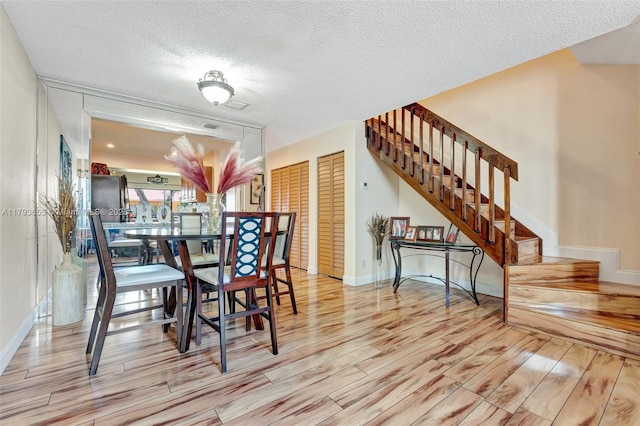 dining area featuring stairway, a textured ceiling, baseboards, and wood finished floors