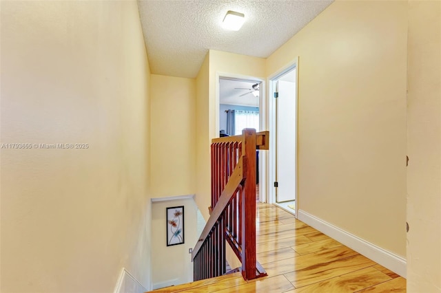 hall with baseboards, light wood-style flooring, a textured ceiling, and an upstairs landing
