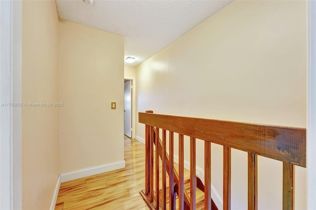 hall featuring baseboards, a textured ceiling, light wood-style flooring, and an upstairs landing