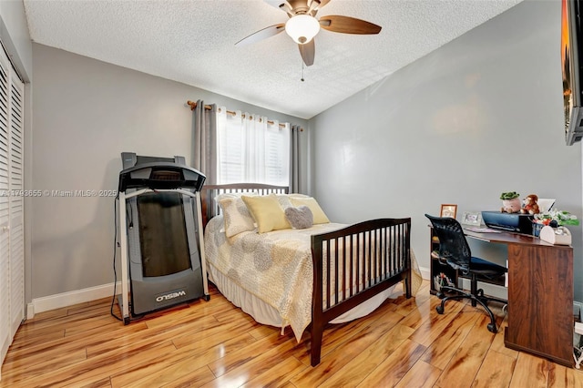 bedroom with a textured ceiling, light wood-style flooring, a ceiling fan, baseboards, and a closet