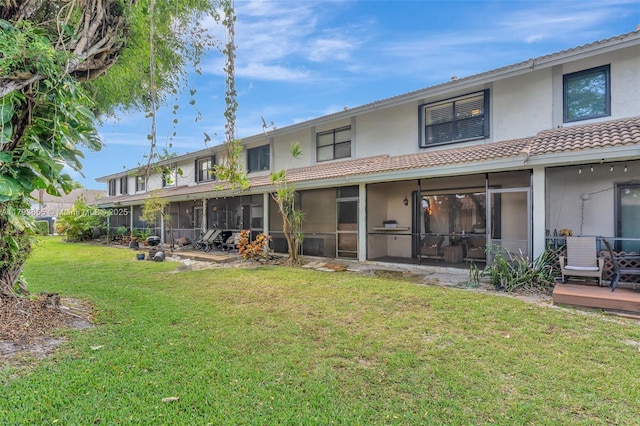 rear view of property featuring a tiled roof, stucco siding, and a yard