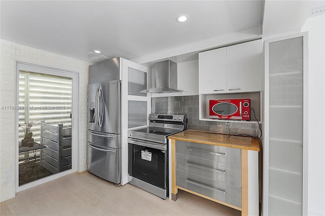 517 NE 38th St Unit 9, Miami, FL 33137 - kitchen featuring stainless steel appliances, wall chimney exhaust hood, light wood-style flooring, white cabinetry, and tasteful backsplash