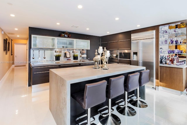 kitchen featuring a kitchen island, a breakfast bar, glass insert cabinets, modern cabinets, and appliances with stainless steel finishes