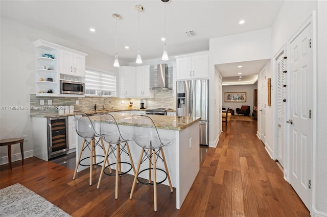 kitchen with a kitchen island, beverage cooler, wall chimney range hood, backsplash, and stainless steel appliances