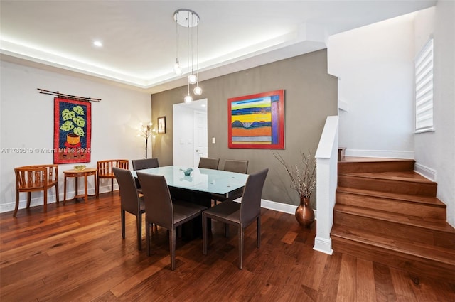 dining space featuring a raised ceiling, baseboards, wood finished floors, and stairway