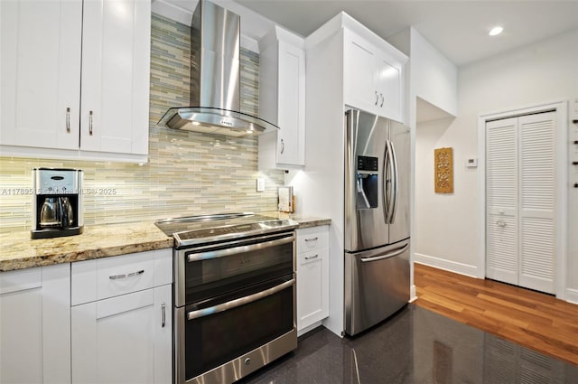 kitchen featuring wall chimney range hood, appliances with stainless steel finishes, tasteful backsplash, baseboards, and white cabinets