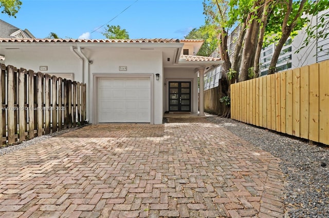 view of front of house featuring french doors, a tile roof, a garage, decorative driveway, and stucco siding