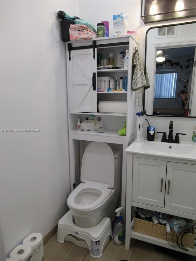 half bathroom featuring visible vents, wood finished floors, toilet, and vanity