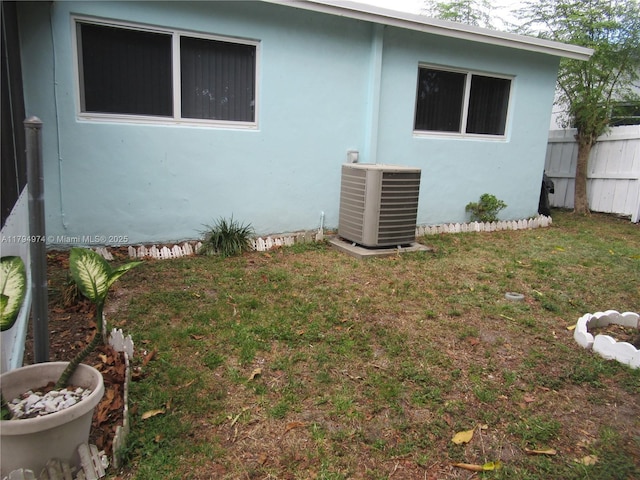 view of side of property featuring a lawn, fence, central AC unit, and stucco siding