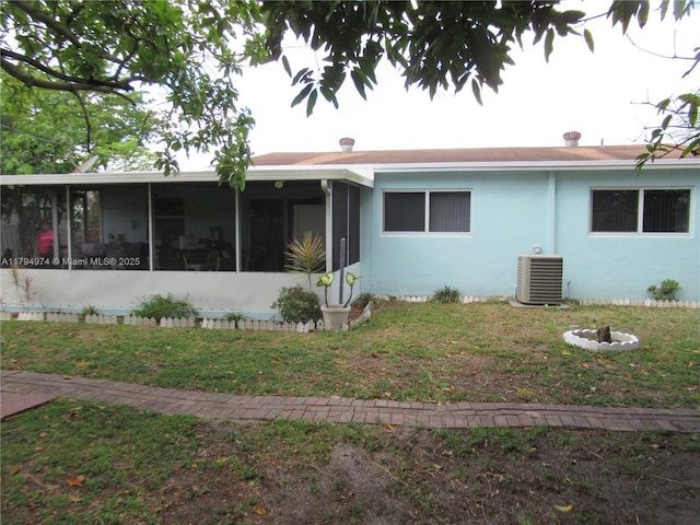 view of front of property with a front yard, central AC unit, a sunroom, and stucco siding