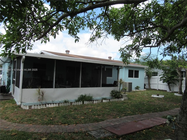 rear view of property with a sunroom, a lawn, central AC, and fence