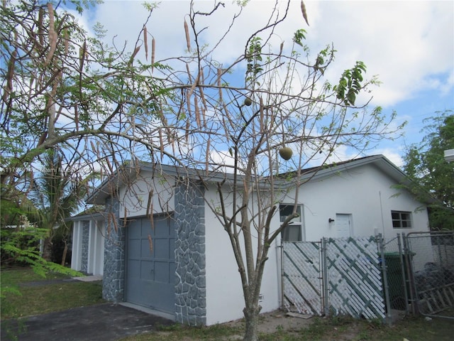 view of side of home featuring driveway, a gate, fence, stone siding, and stucco siding