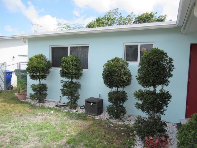view of property exterior featuring a lawn, stucco siding, and fence