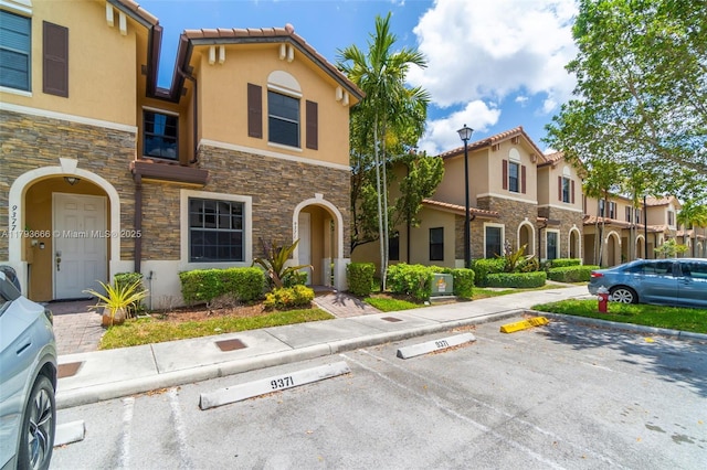 mediterranean / spanish home with stone siding, a tiled roof, stucco siding, and uncovered parking