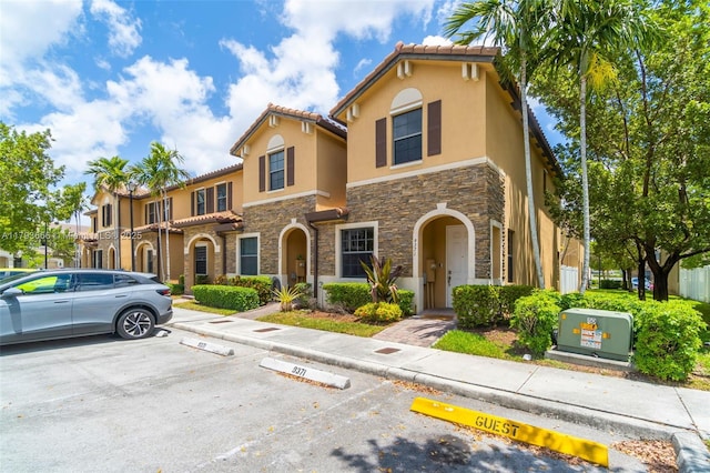 mediterranean / spanish-style home with stone siding, stucco siding, a tiled roof, and uncovered parking