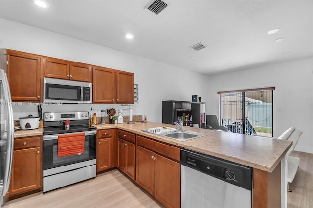 kitchen with light wood-type flooring, a peninsula, appliances with stainless steel finishes, and a sink