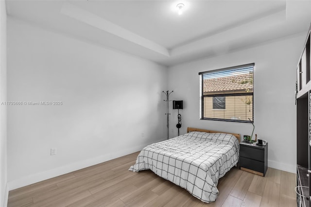 bedroom with baseboards, light wood finished floors, and a tray ceiling