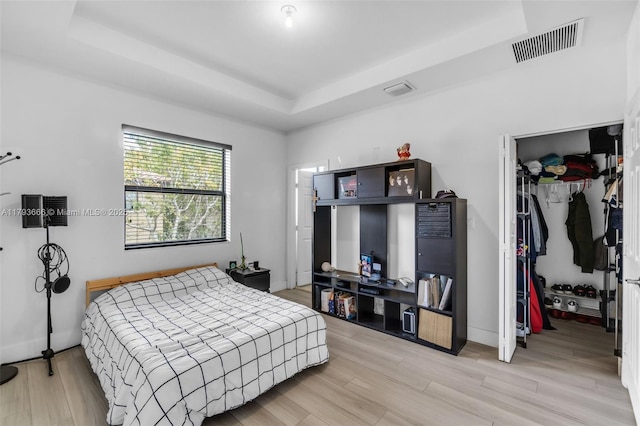 bedroom with a closet, visible vents, light wood finished floors, a tray ceiling, and a walk in closet