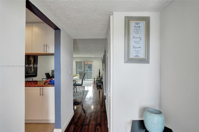 hall featuring baseboards, a textured ceiling, and wood finished floors