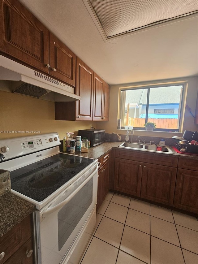 kitchen with dark countertops, a sink, light tile patterned floors, under cabinet range hood, and white electric range