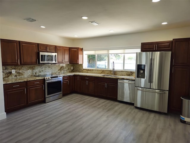 kitchen featuring decorative backsplash, appliances with stainless steel finishes, light wood-type flooring, a sink, and light stone counters