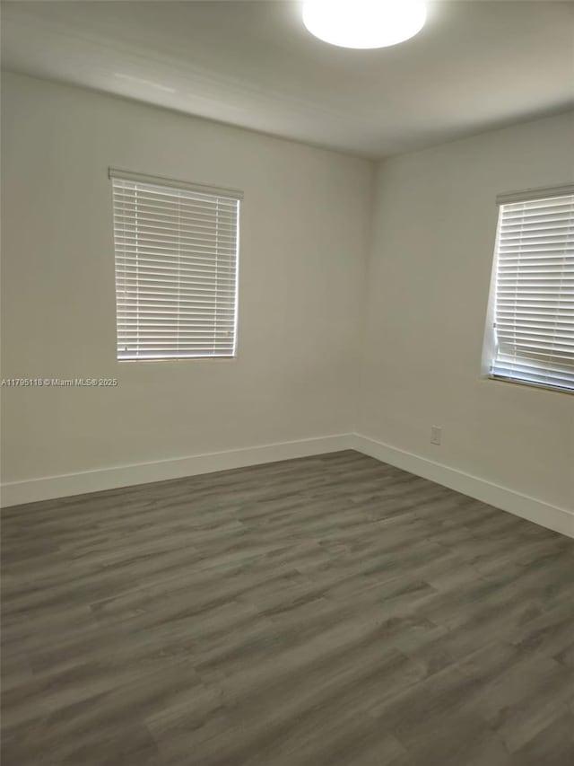 spare room featuring baseboards and dark wood-style flooring