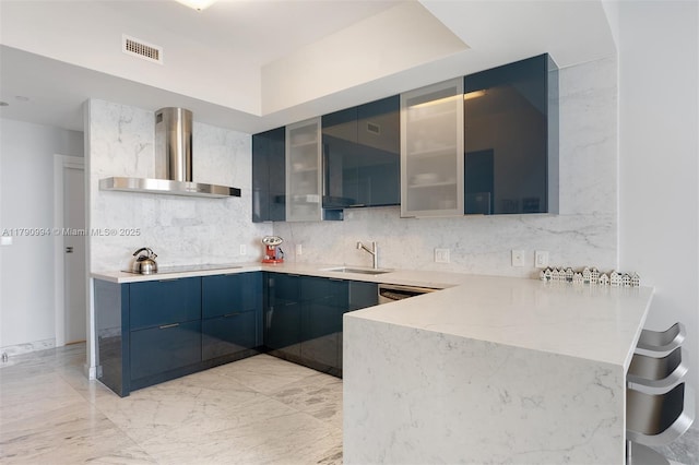 kitchen featuring a peninsula, glass insert cabinets, modern cabinets, wall chimney range hood, and a sink