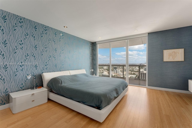 bedroom featuring access to outside, wallpapered walls, wood finished floors, and expansive windows