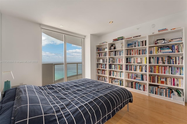 bedroom with access to outside, recessed lighting, wood finished floors, and expansive windows